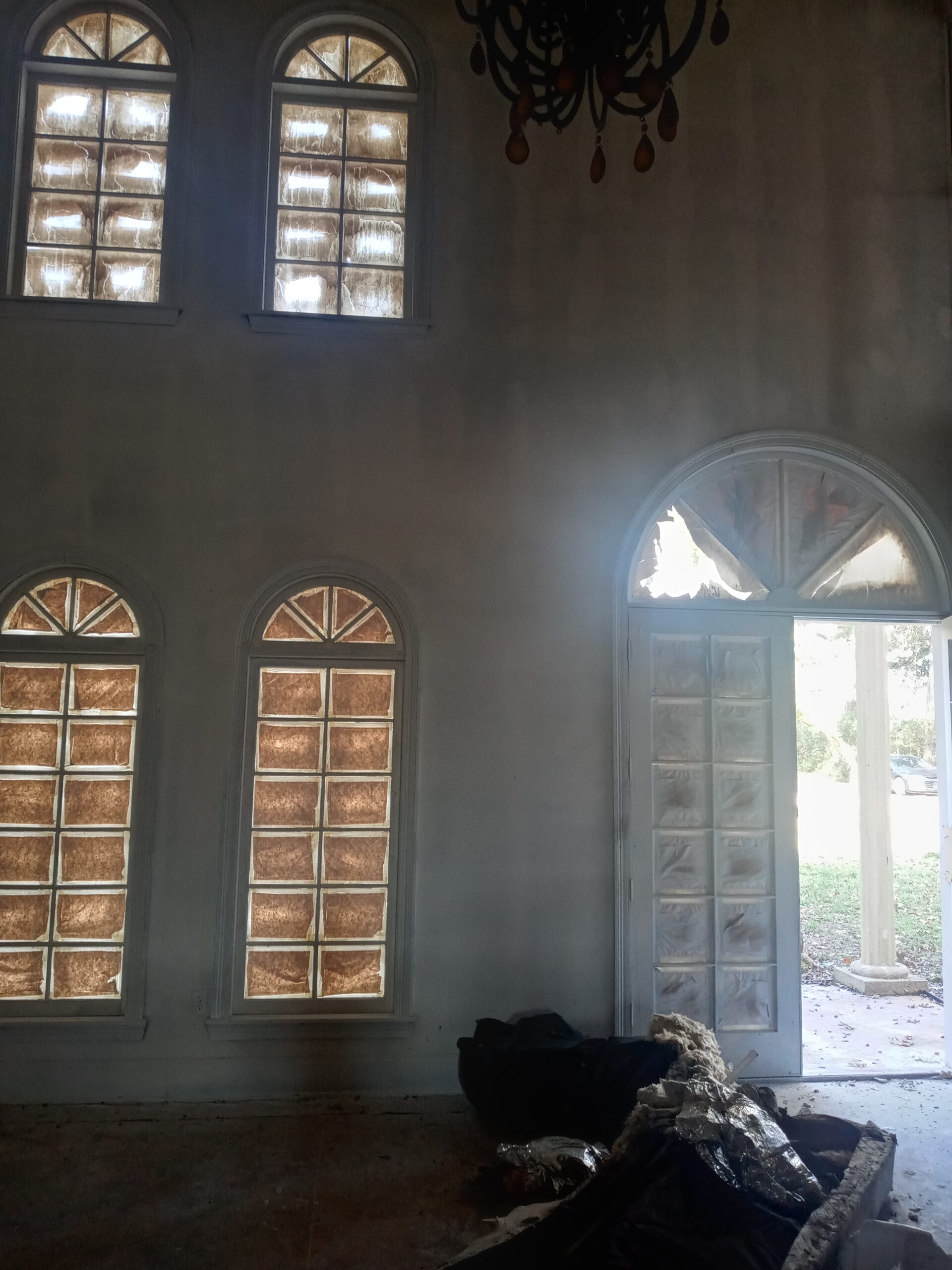 An interior space with large glass block windows, a double door entrance, and remnants of furniture scattered on the floor.