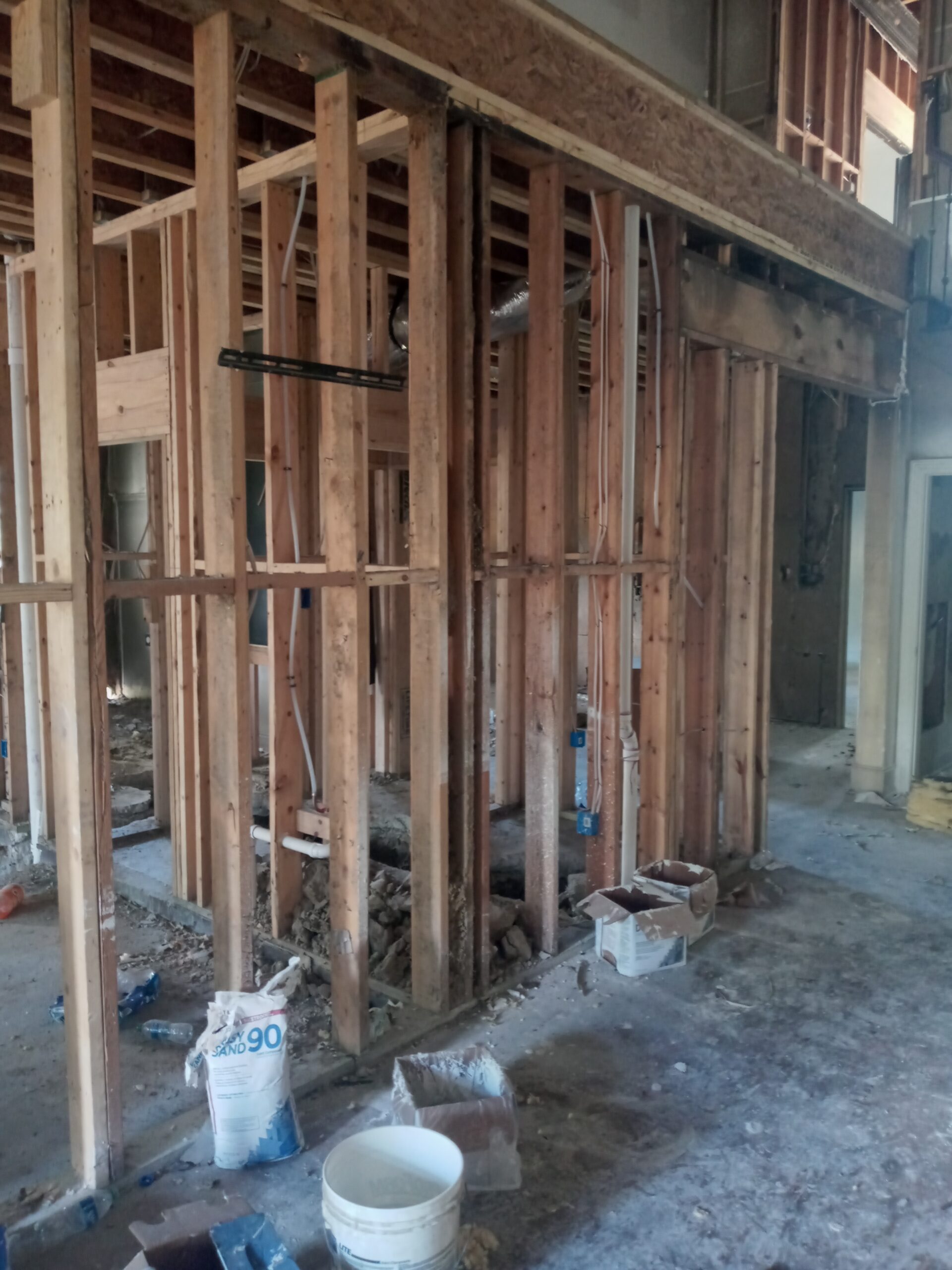 An interior construction site showing exposed wooden framing, debris on the floor, and various construction materials scattered around.