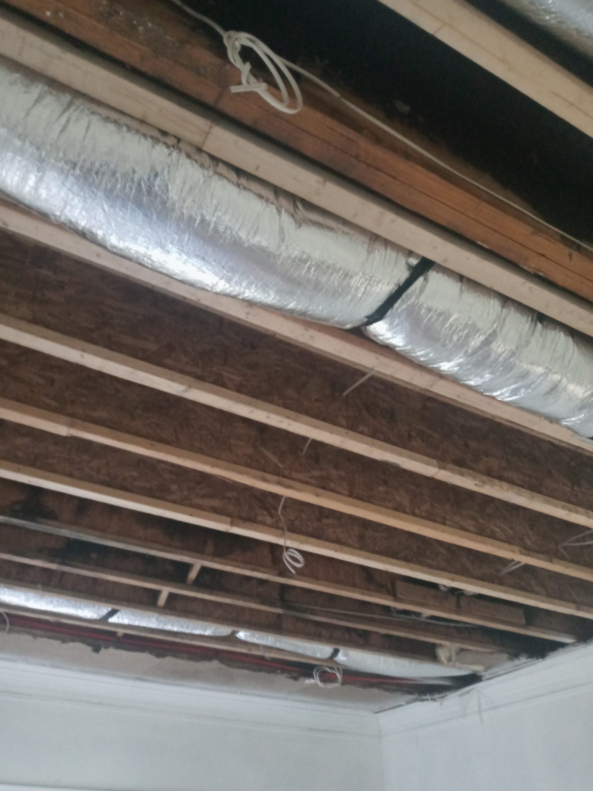 Exposed ceiling with wooden beams and visible ductwork, showcasing construction elements and potential renovation work.