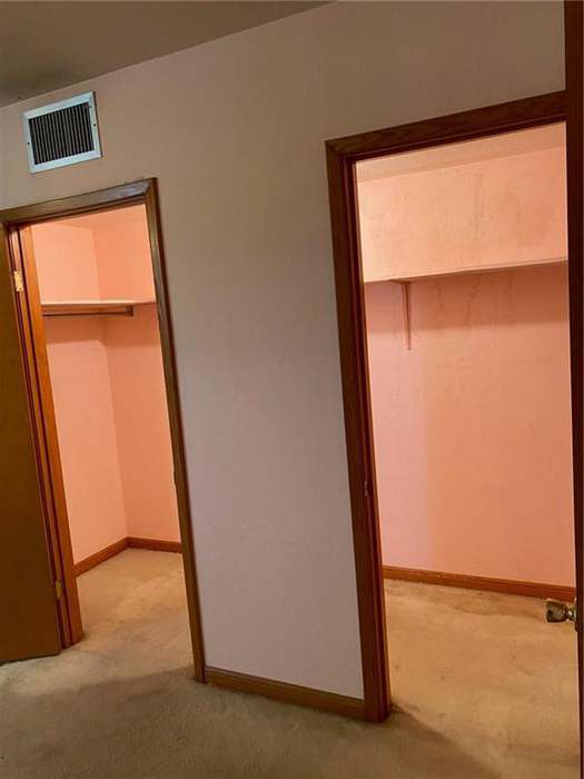A room featuring two doorways leading to closets, with pink walls and carpeted flooring.
