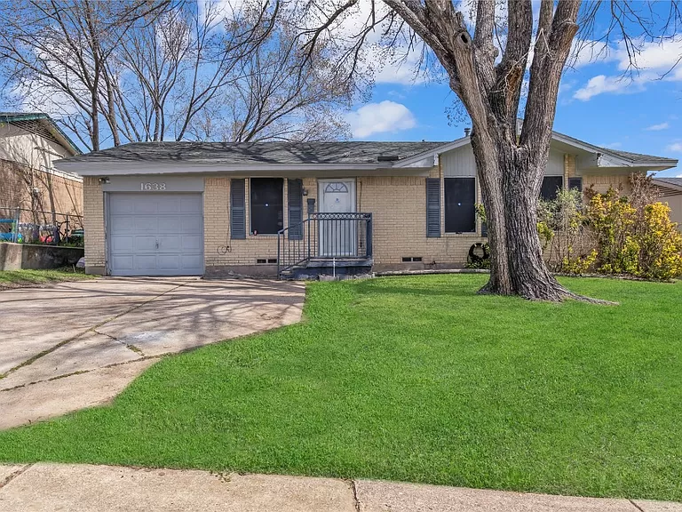 A single-story house with a garage, surrounded by a lush green lawn and large trees under a clear blue sky.