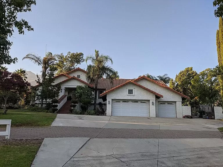 A large residential house with a red-tiled roof, surrounded by palm trees and a well-maintained yard, featuring a driveway and garage.