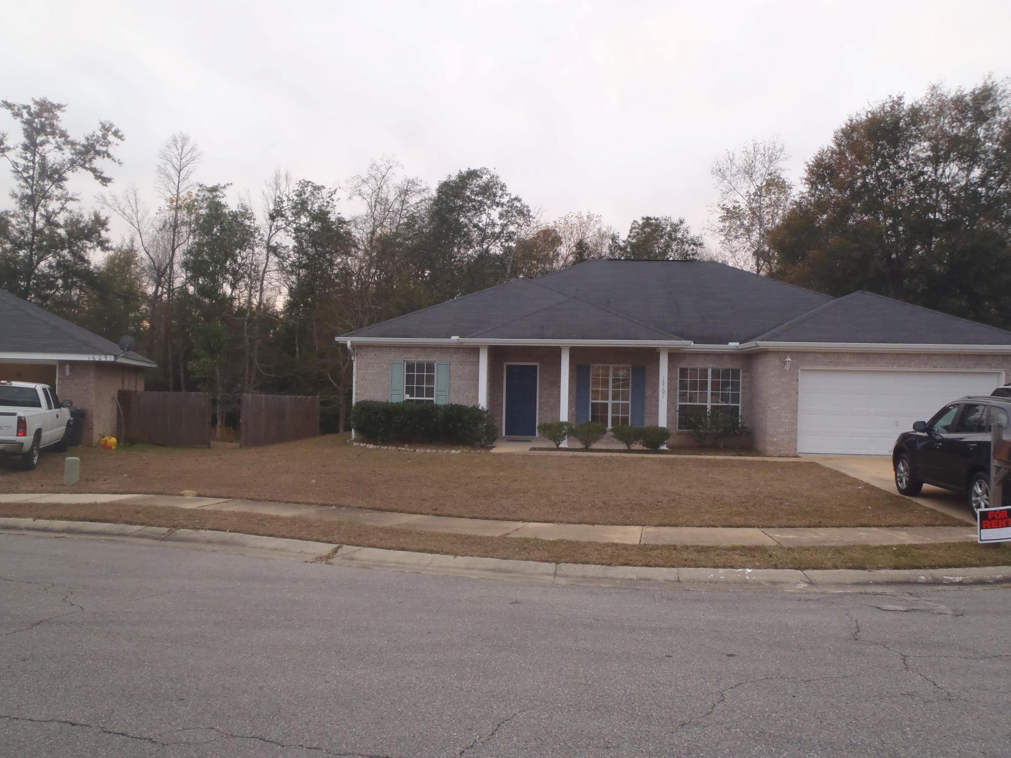 A suburban house with a blue door, surrounded by sparse landscaping and visible vehicles parked on the street.