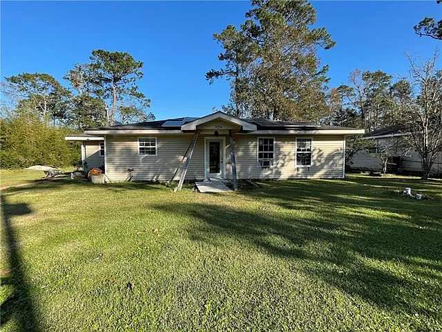 A single-story house surrounded by green grass and trees under a clear blue sky.