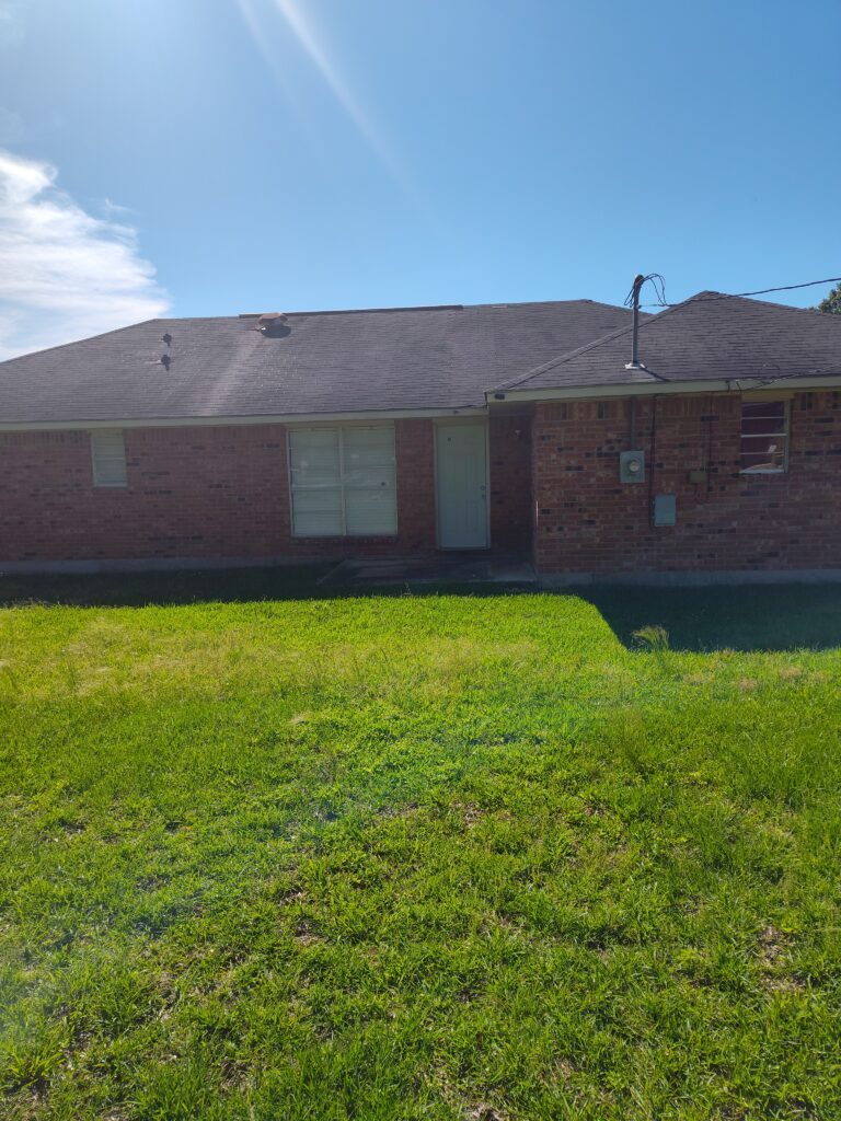 A brick house with a grassy yard under a clear blue sky.